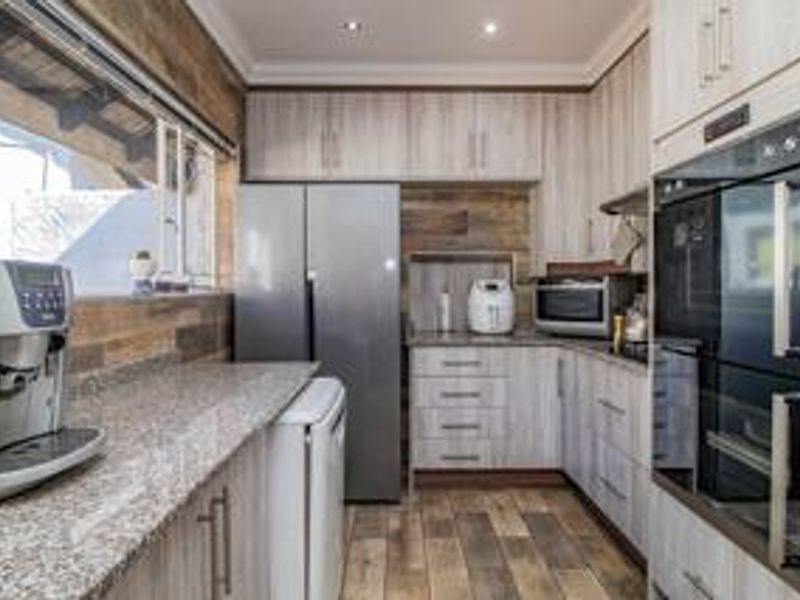 A modern kitchen featuring light wood-grain cabinetry, granite countertops, built-in double ovens, and tiled flooring with recessed lighting.