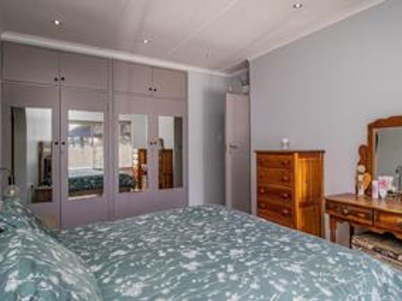 A well-maintained bedroom featuring extensive built-in cupboards with mirrored panels, recessed downlighting, and coved ceiling finishes.