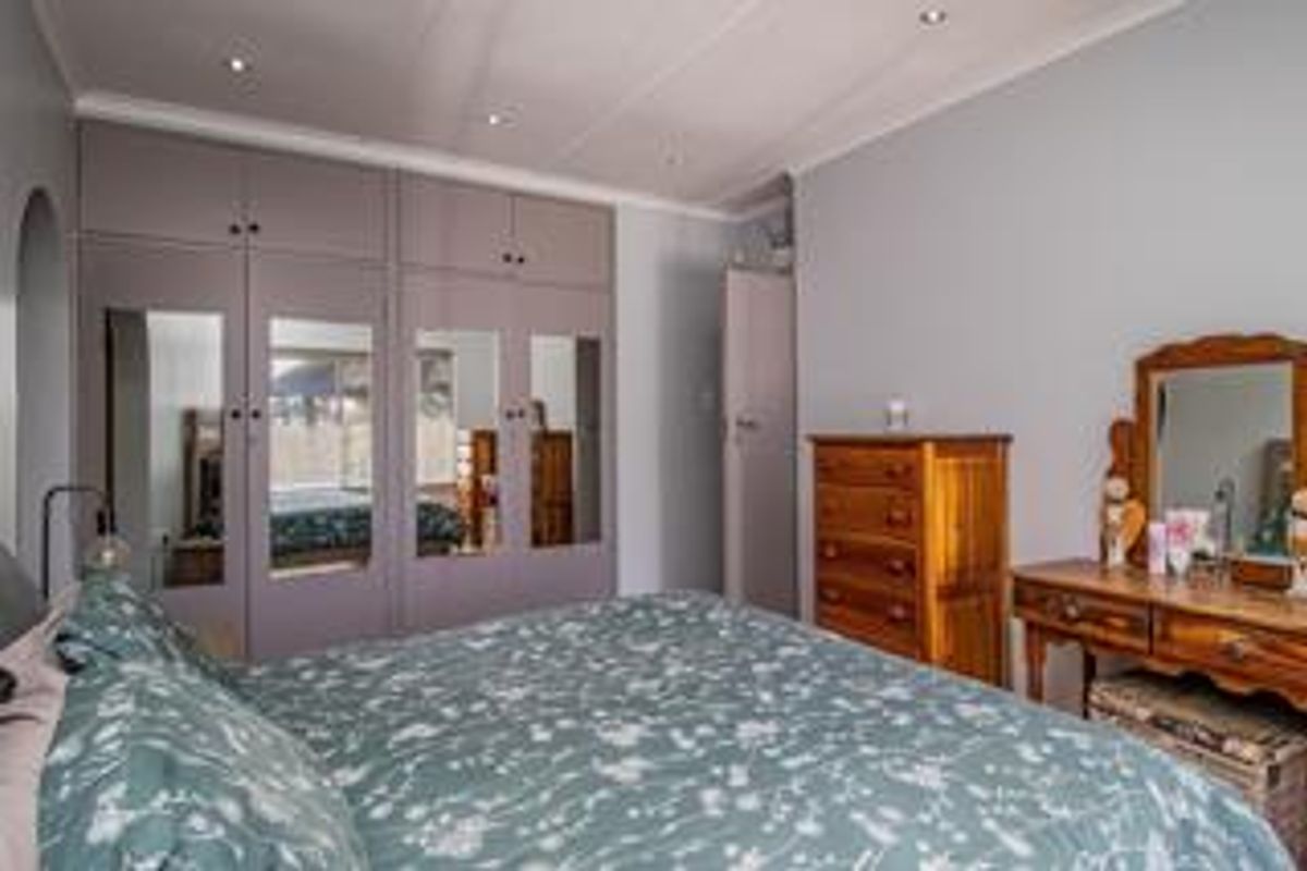 A well-maintained bedroom featuring extensive built-in cupboards with mirrored panels, recessed downlighting, and coved ceiling finishes.