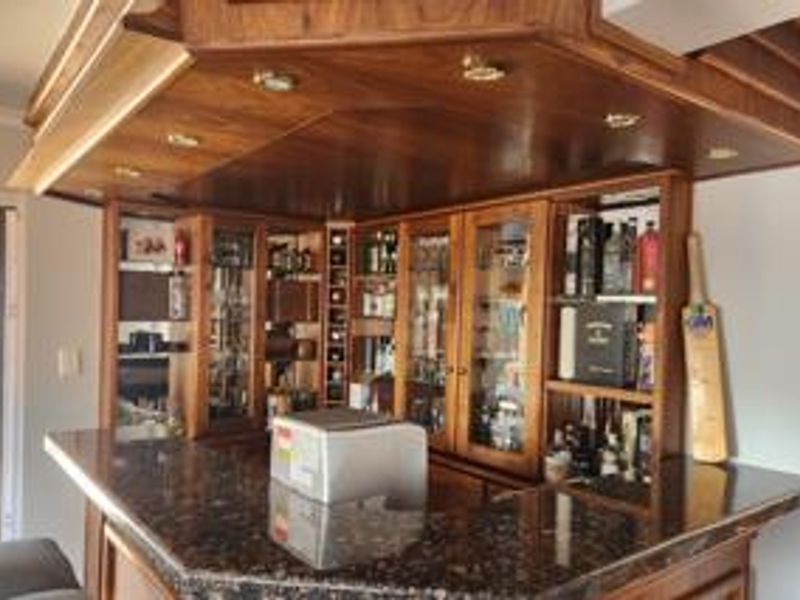 A custom-built wooden home bar featuring a granite countertop, integrated glass display cabinetry, mirrored backing, and recessed ceiling lighting.