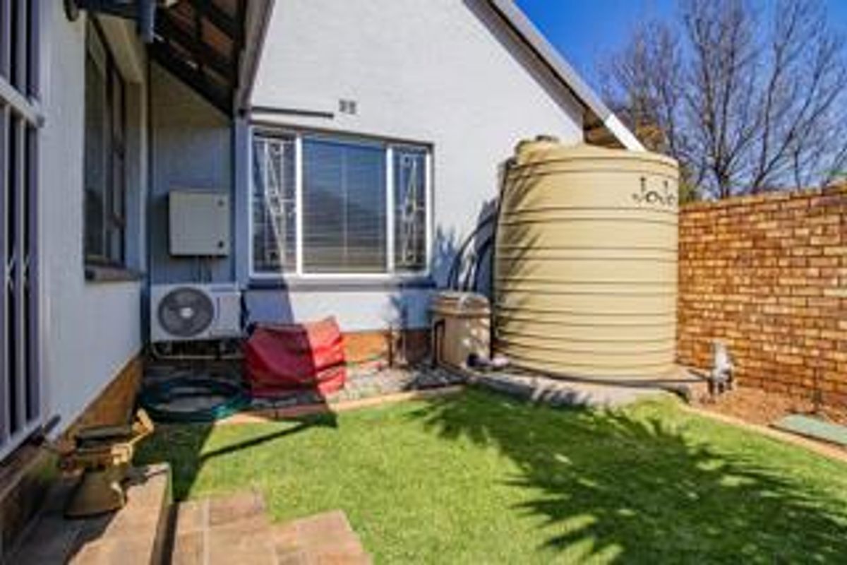Rear exterior view featuring a water storage tank, air conditioning unit, and a small lawn area enclosed by a brick boundary wall.
