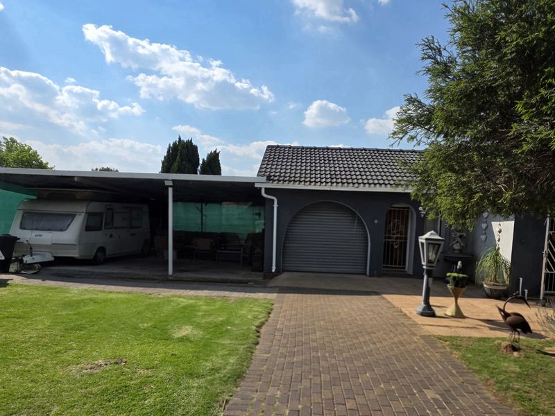 Rear exterior view featuring a paved driveway, a large carport structure, a roller shutter garage door, and a well-maintained lawn area.