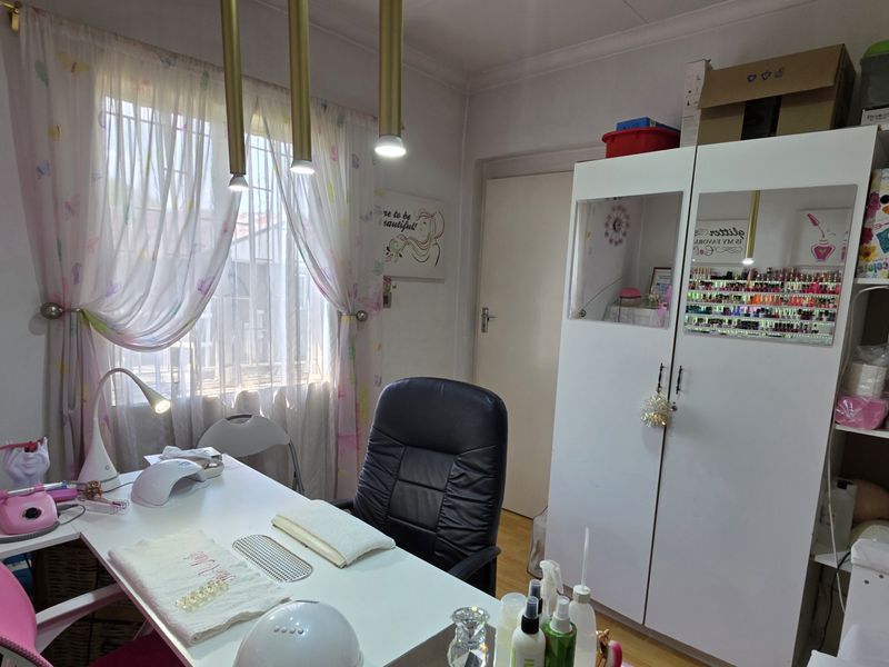 A bedroom currently utilized as a home salon, featuring laminate flooring, built-in cupboard storage, and pendant lighting.