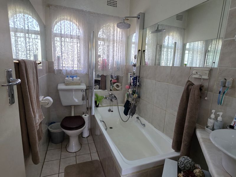 A functional bathroom featuring a bathtub with shower attachment, a toilet, and a vanity basin, finished with neutral wall and floor tiling.