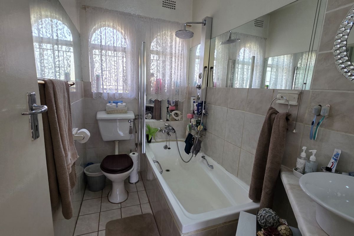 A functional bathroom featuring a bathtub with shower attachment, a toilet, and a vanity basin, finished with neutral wall and floor tiling.