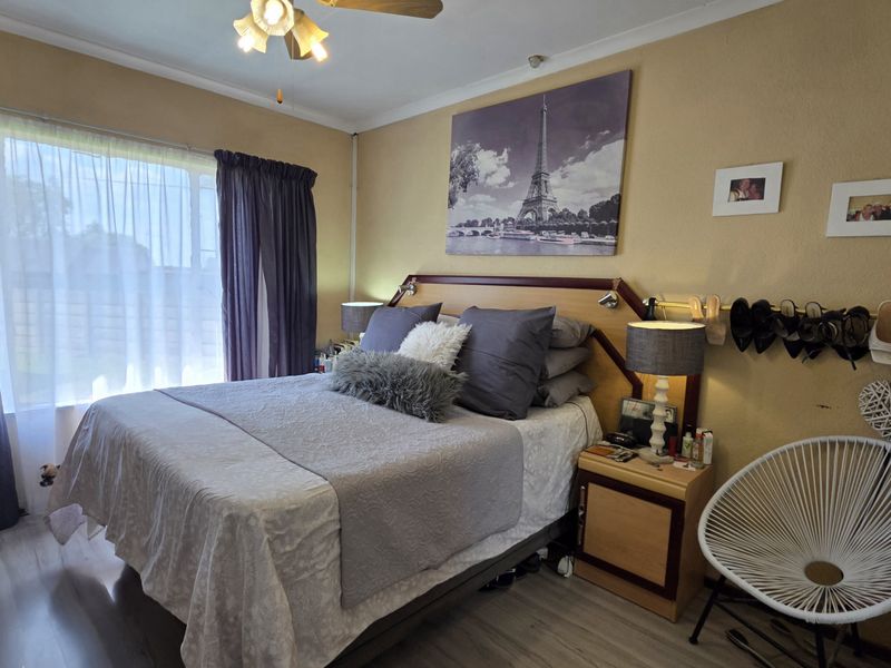 A comfortable bedroom featuring laminate flooring, a ceiling fan, and a built-in headboard, offering a functional and well-lit living space.