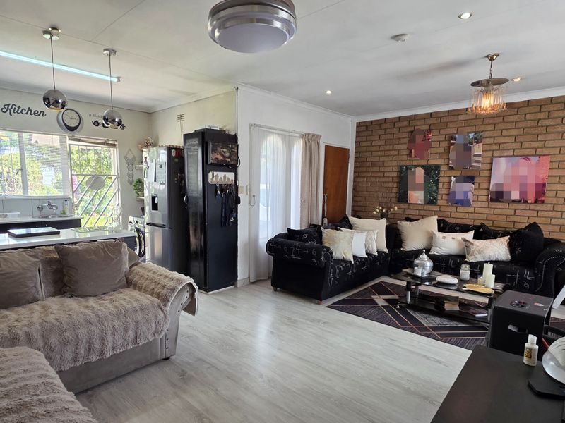 Open-plan living area featuring a prominent exposed brick wall, laminate flooring, and an integrated kitchen space with a central island.