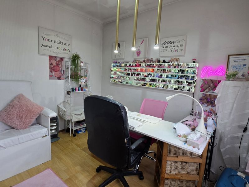 A functional utility space currently utilized as a nail salon, featuring laminate flooring and modern pendant lighting.