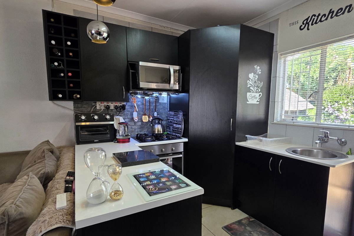 Compact kitchen featuring dark cabinetry, built-in oven, hob, extractor fan, microwave, and a stainless steel sink with a tiled backsplash.