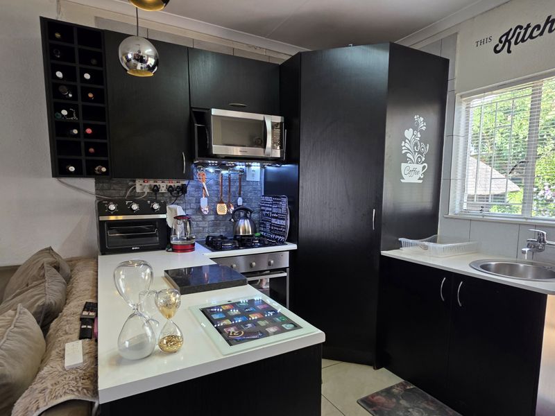 Compact kitchen featuring dark cabinetry, built-in oven, hob, extractor fan, microwave, and a stainless steel sink with a tiled backsplash.