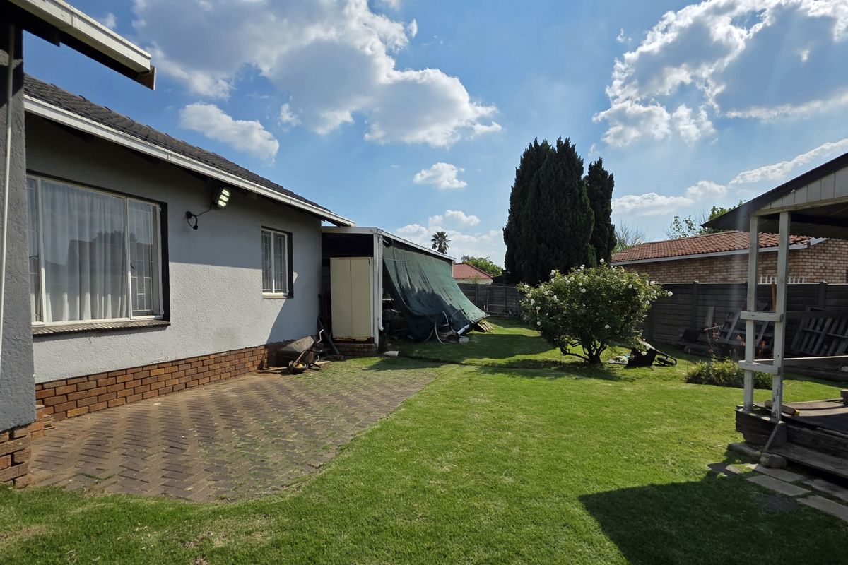 Rear garden area featuring a paved patio, established lawn, and a covered outdoor structure, enclosed by a perimeter wall.
