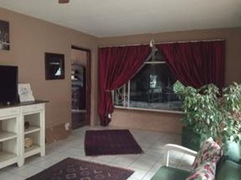 A living room featuring tiled flooring, a large window with curtains, and a ceiling fan, offering a functional space for relaxation.