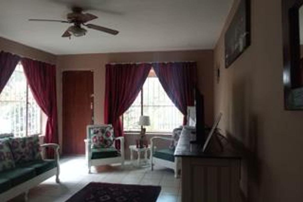 A living room featuring tiled flooring, a ceiling fan, and windows fitted with security bars.