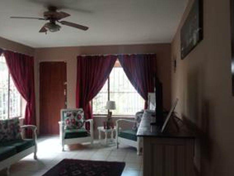 A living room featuring tiled flooring, a ceiling fan, and windows fitted with security bars.