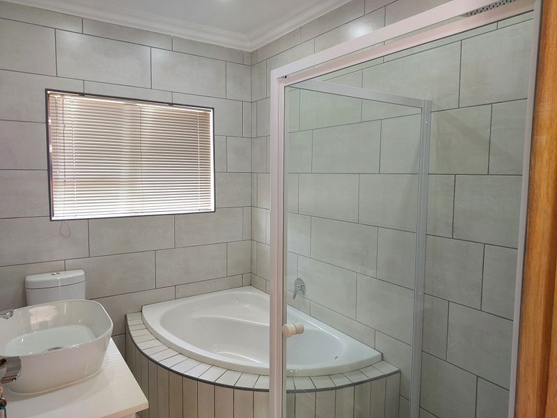 A modern bathroom featuring a corner bathtub, glass shower enclosure, and a contemporary vessel sink with neutral wall tiling.