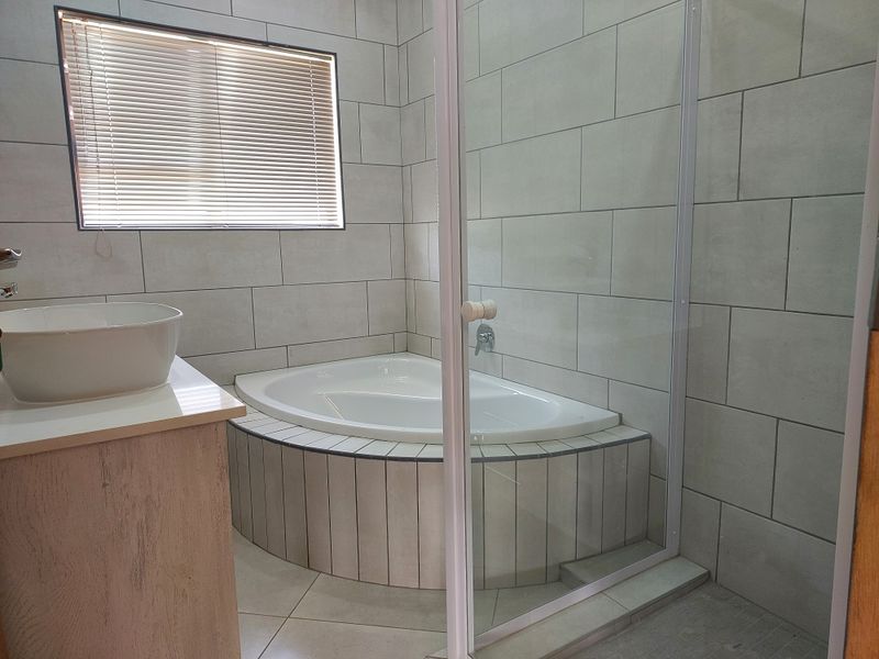 Modern bathroom featuring a corner bathtub, glass-enclosed shower, and a vanity with a vessel sink, finished with neutral wall and floor tiles.