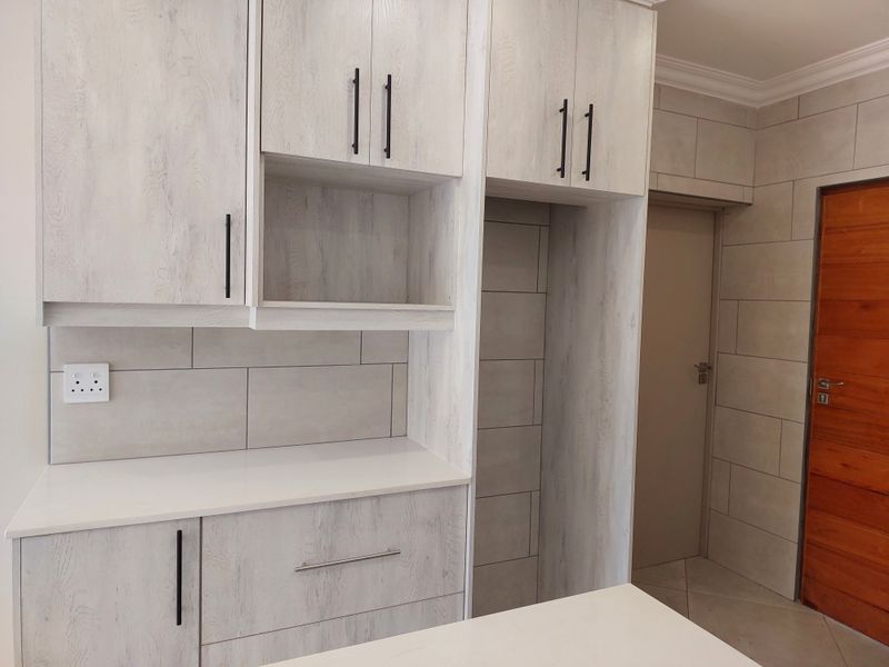 Modern kitchen area featuring light wood-grain cabinetry, stone countertops, and neutral tiled finishes, providing a clean and contemporary aesthetic.