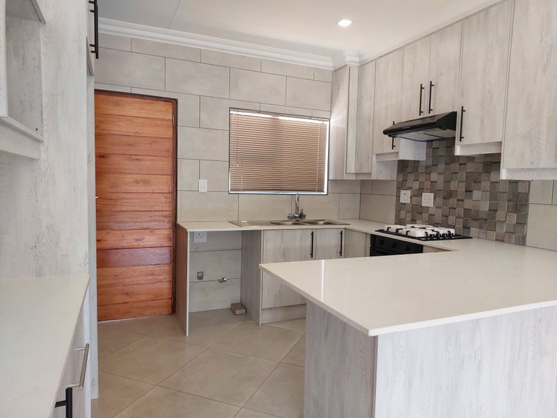 Modern kitchen featuring light wood-grain cabinetry, stone countertops, a gas hob with extractor fan, and neutral tiled finishes throughout.