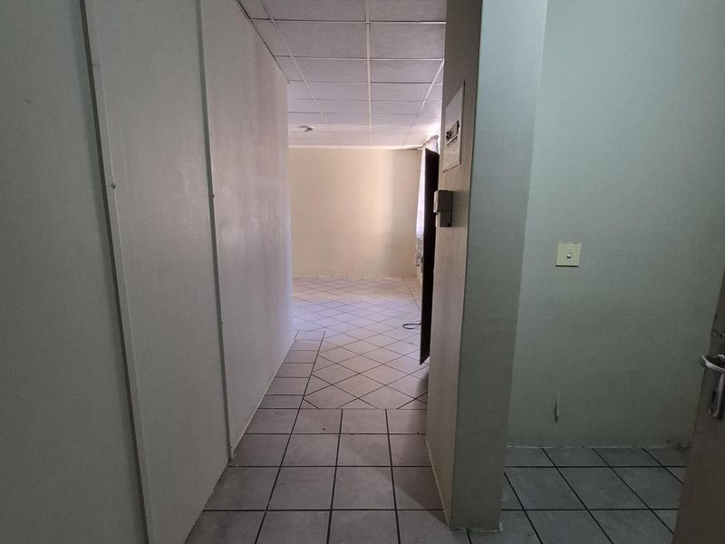 A vacant hallway featuring tiled flooring and a drop ceiling, leading into an adjacent living space.