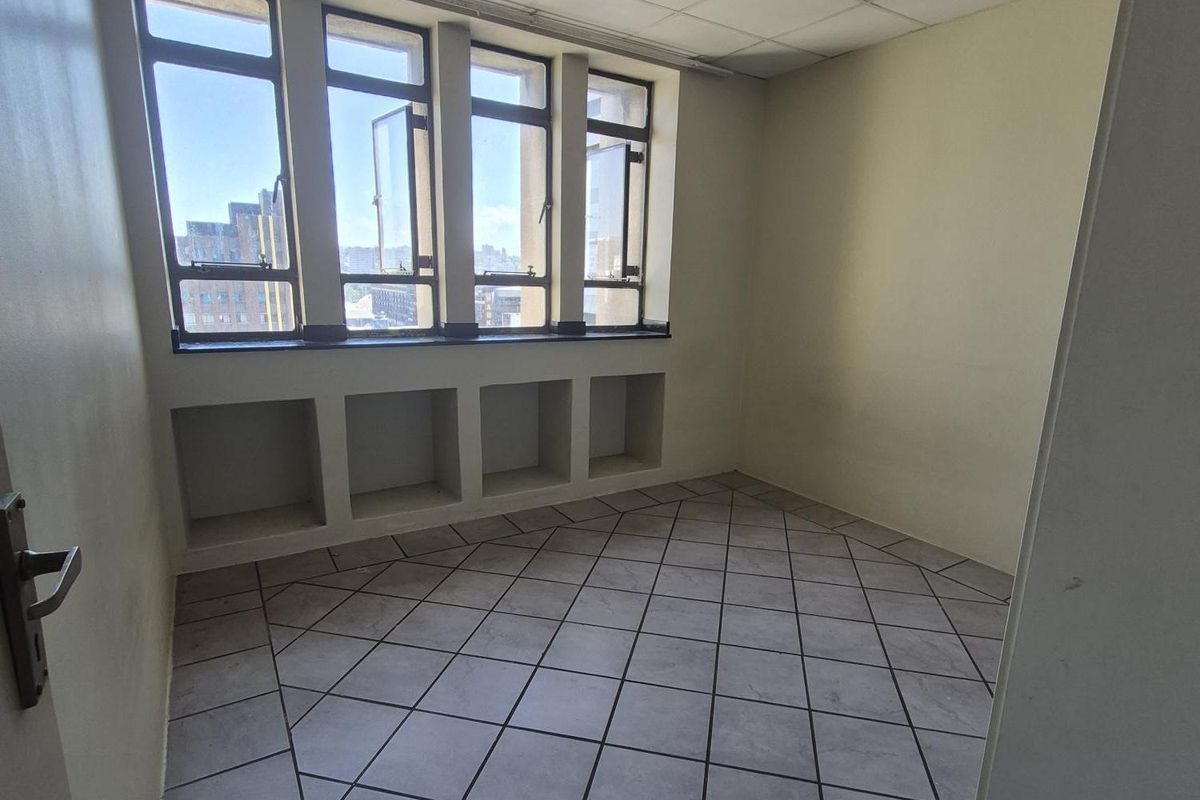 An empty bedroom featuring tiled flooring, a drop ceiling, and built-in shelving under large casement windows with city views.
