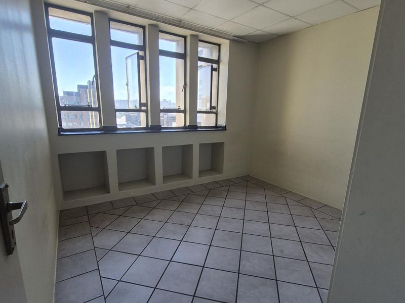 An empty bedroom featuring tiled flooring, a drop ceiling, and built-in shelving under large casement windows with city views.