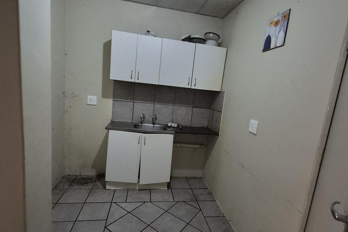 A compact kitchen area featuring basic built-in cabinetry, a stainless steel sink, tiled backsplash, and ceramic floor tiles, requiring cosmetic updates.