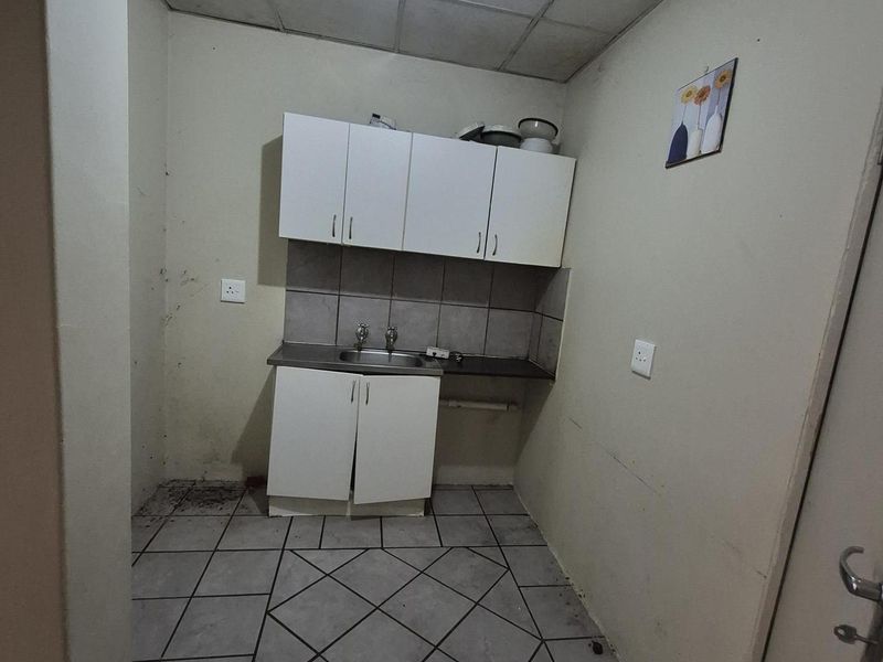 A compact kitchen area featuring basic built-in cabinetry, a stainless steel sink, tiled backsplash, and ceramic floor tiles, requiring cosmetic updates.