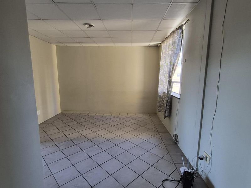 An empty living room featuring ceramic tile flooring and a drop ceiling, offering a blank canvas for renovation and interior design updates.