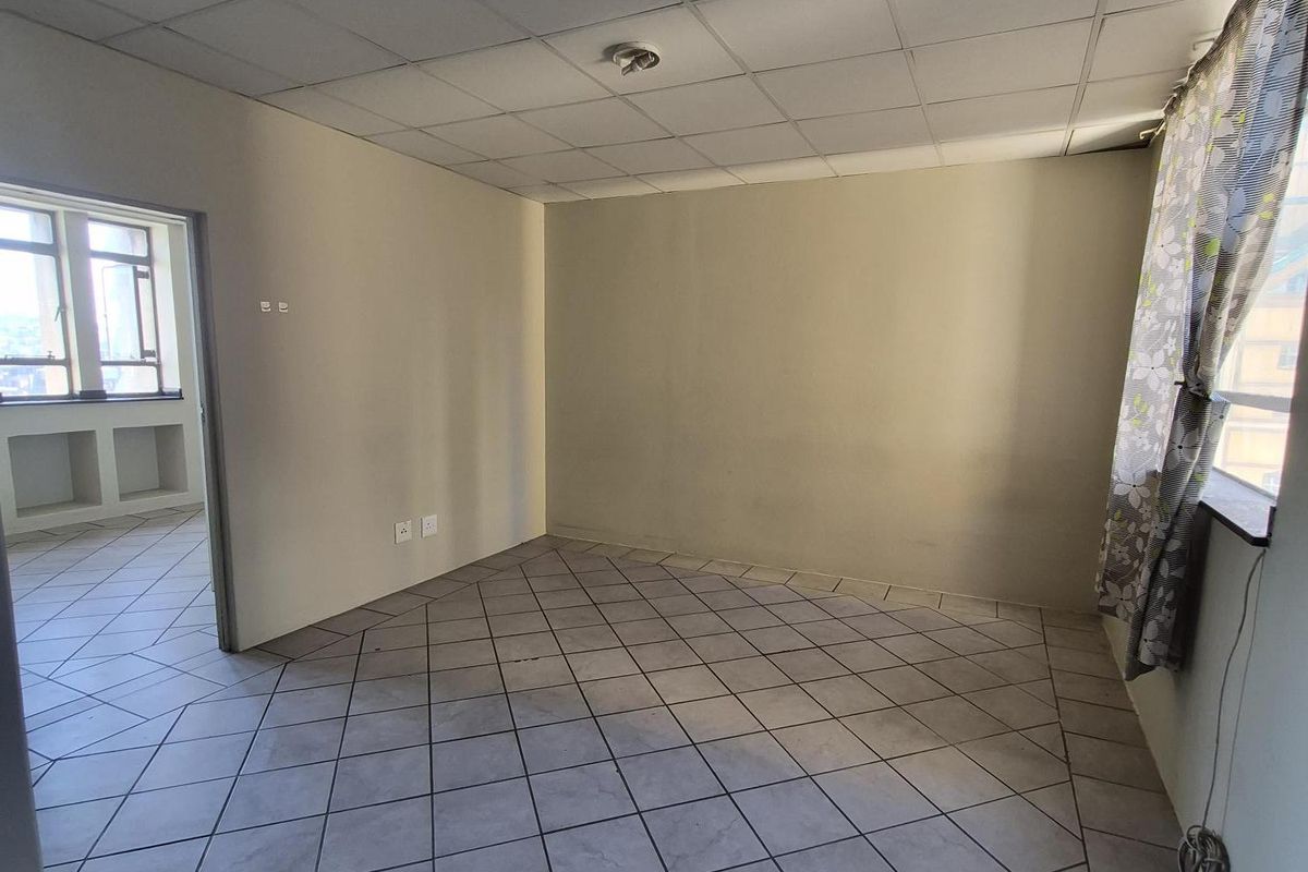 An empty living room featuring tiled flooring and a drop ceiling, with an adjacent room visible through the doorway.