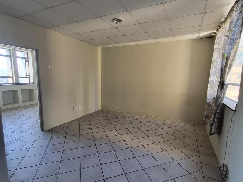 An empty living room featuring tiled flooring and a drop ceiling, with an adjacent room visible through the doorway.