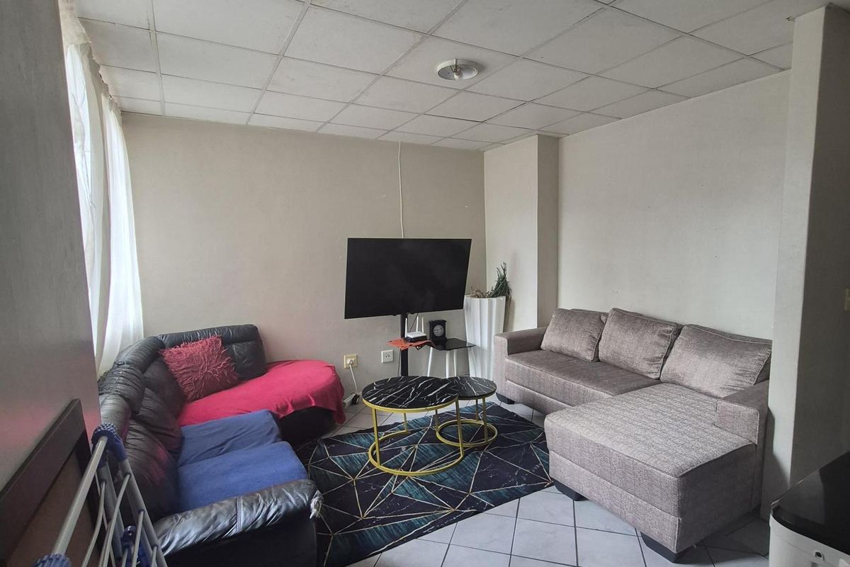 A living room area featuring tiled flooring and a suspended ceiling, offering a functional space that could benefit from cosmetic updates.