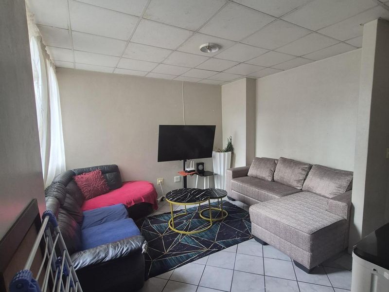 A living room area featuring tiled flooring and a suspended ceiling, offering a functional space that could benefit from cosmetic updates.