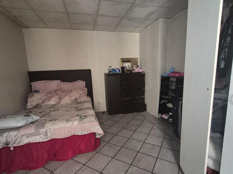 A bedroom featuring tiled flooring and a drop ceiling with visible signs of wear and staining, including a built-in wardrobe.
