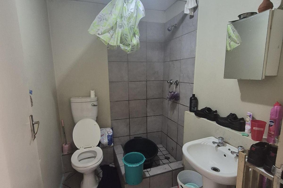 A functional bathroom featuring a pedestal basin, toilet, and a tiled shower cubicle with a drop ceiling.
