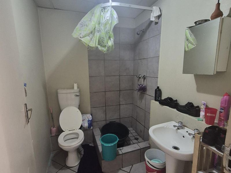 A functional bathroom featuring a pedestal basin, toilet, and a tiled shower cubicle with a drop ceiling.