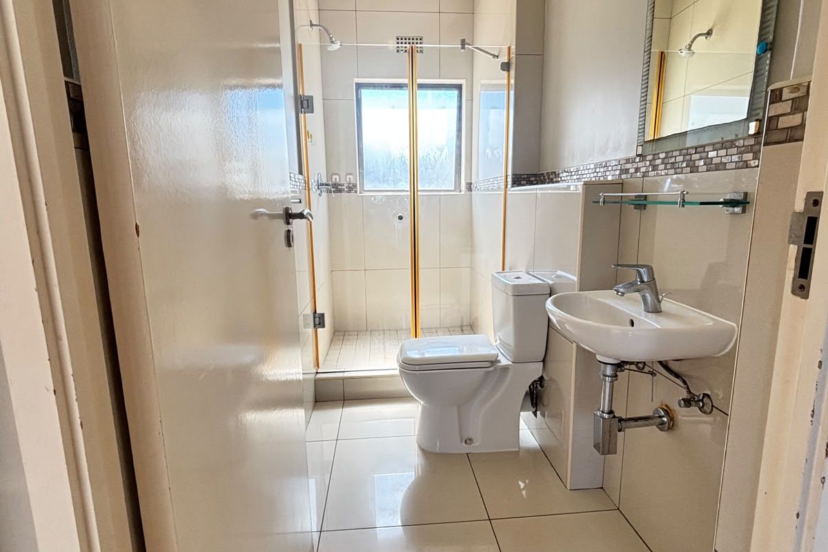 A compact, functional bathroom featuring a shower enclosure, wall-mounted basin, and neutral floor-to-ceiling tiling.