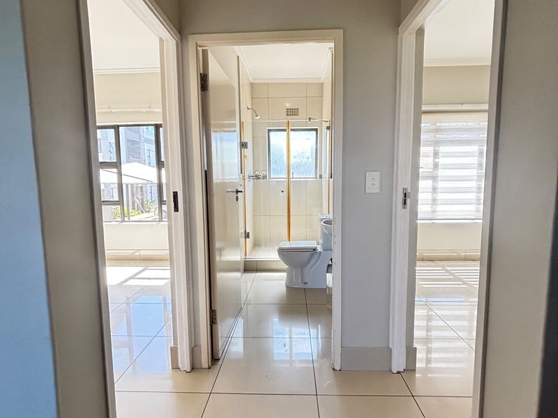 A bright, tiled hallway providing access to adjacent rooms, including a bathroom with a shower and two other living spaces.