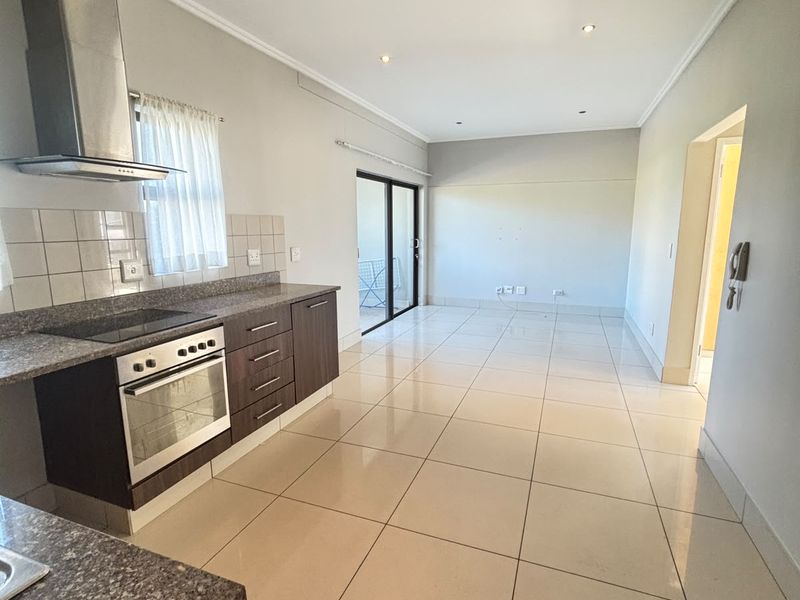 Spacious open-plan kitchen and living area featuring tiled floors, modern cabinetry, granite countertops, and direct access to an outdoor space via sliding glass doors.
