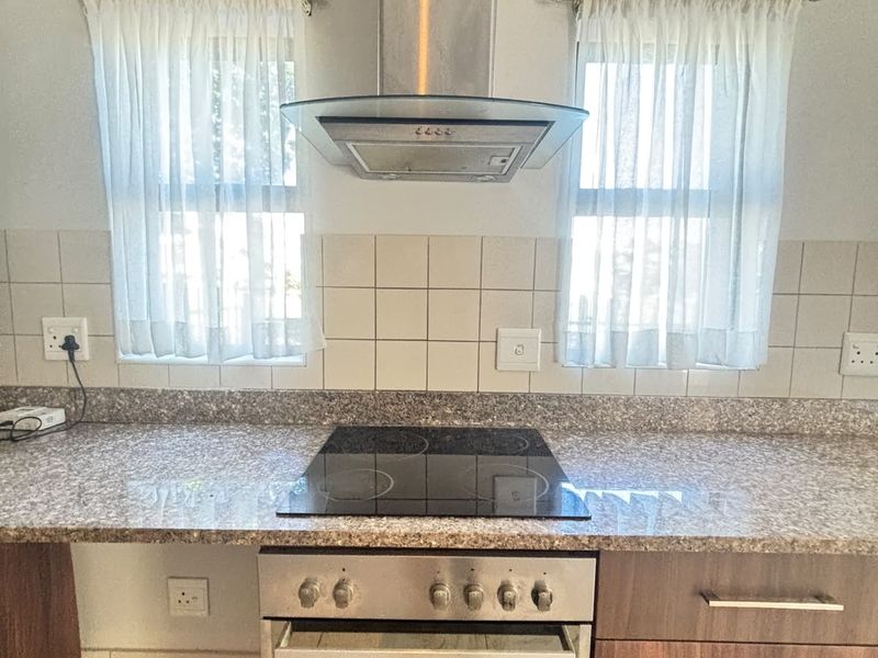 A functional kitchen area featuring a built-in oven, electric hob, stainless steel extractor fan, and granite countertops with tiled backsplash.