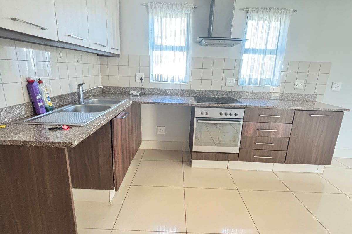A clean and functional kitchen featuring granite countertops, built-in cabinetry, a stainless steel oven, hob, and extractor fan with neutral tiled flooring.