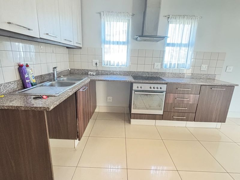 A clean and functional kitchen featuring granite countertops, built-in cabinetry, a stainless steel oven, hob, and extractor fan with neutral tiled flooring.