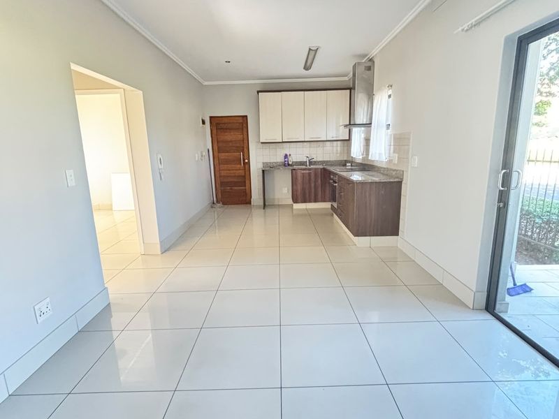 Spacious open-plan kitchen and living area featuring modern tiled flooring, built-in cabinetry with granite countertops, and direct access to an outdoor patio.