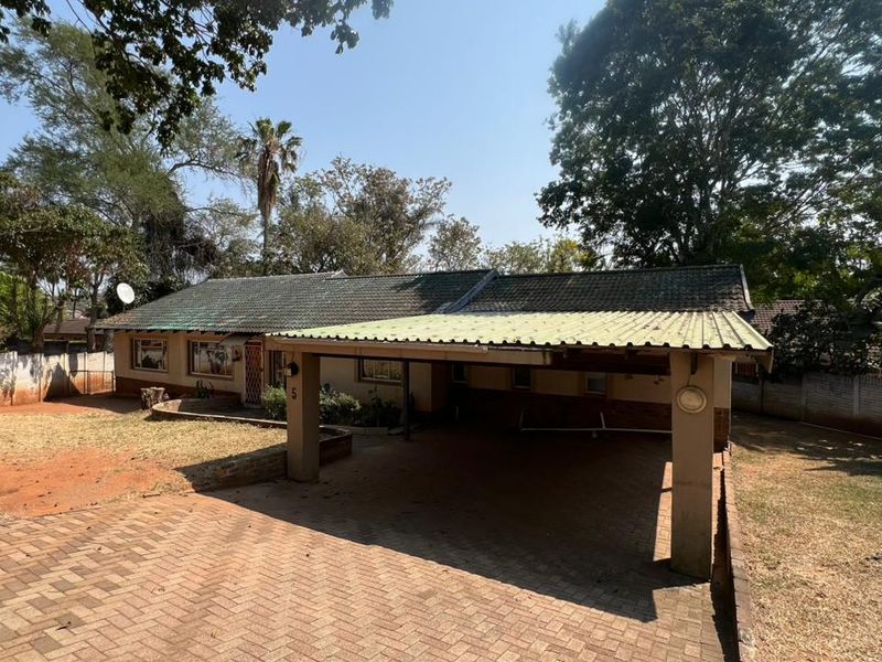 Front view of a single-story house featuring a paved driveway, attached carport, and established garden surroundings.