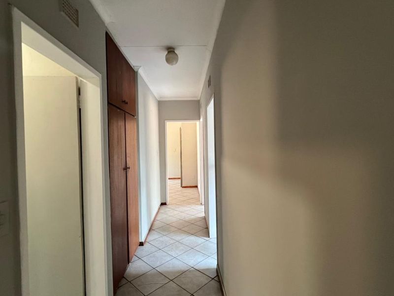 A clean, functional hallway featuring tiled flooring and built-in wooden storage cupboards, providing access to multiple rooms within the home.