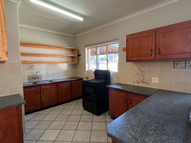 A functional kitchen featuring wooden cabinetry, laminate countertops, tiled backsplash, and ceramic flooring, offering a classic layout with ample storage space.