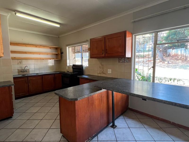 A spacious, dated kitchen featuring wooden cabinetry, laminate countertops, a breakfast bar, and ceramic floor tiles, offering significant potential for modernization.