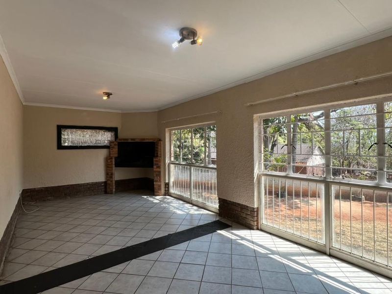 Spacious living area featuring tiled flooring, a built-in brick fireplace, and large windows with security bars overlooking the garden.