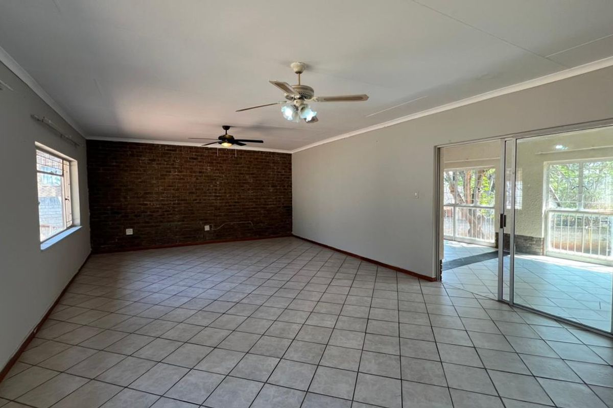 Spacious living area featuring an exposed brick accent wall, tiled flooring, dual ceiling fans, and direct access to an adjoining patio through sliding glass doors.