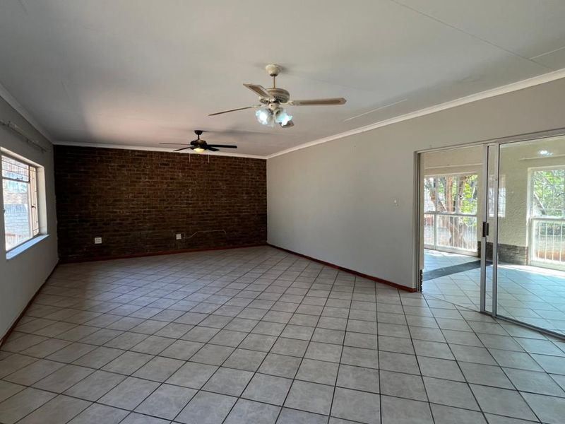 Spacious living area featuring an exposed brick accent wall, tiled flooring, dual ceiling fans, and direct access to an adjoining patio through sliding glass doors.