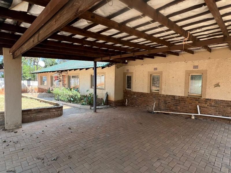 A covered outdoor patio area featuring brick paving, a timber pergola structure, and direct access to the rear garden and main house exterior.